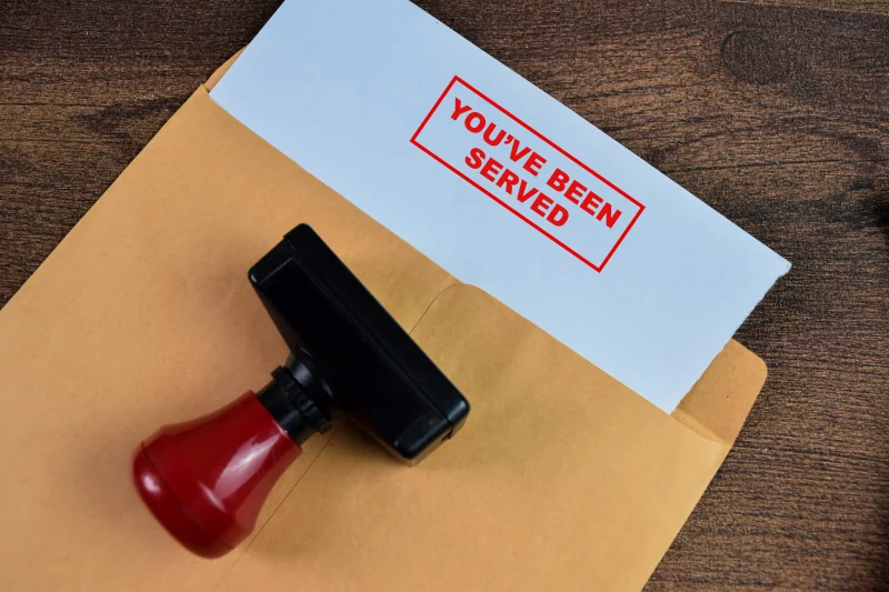 A stock photo illustrating the legal concept of process serving, featuring a rubber stamp with a red handle and a stamped document in a manila envelope